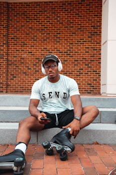 Man sitting with roller skates and smartphone, listening to music outdoors.