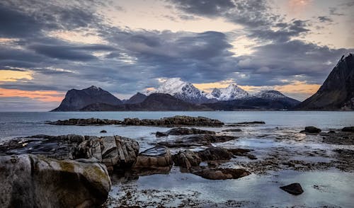 Snowy rocks and sea under cloudy sky in evening