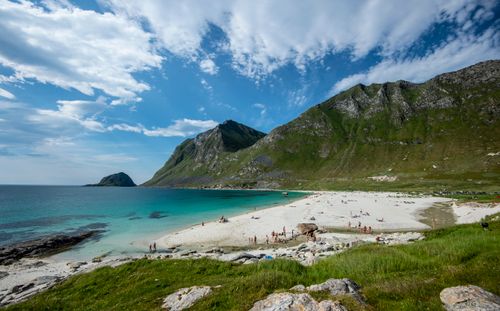 Free Scenic view of ocean shore with unrecognizable tourists near mossy mountain under bright cloudy sky Stock Photo