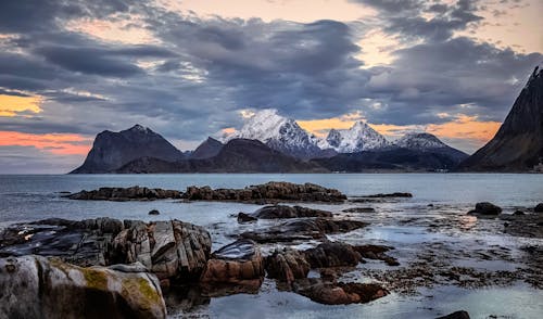 Scenic view of rough rocks near endless ocean under bright cloudy sky at sunset