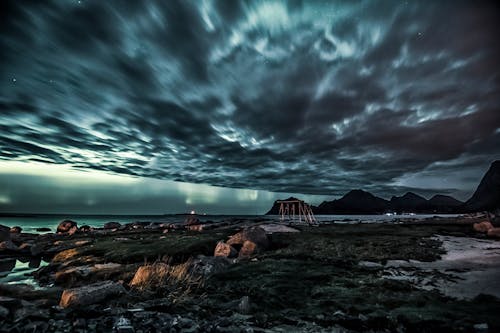 Scenic view of ocean near mountain silhouettes under cloudy sky at sunset in overcast weather