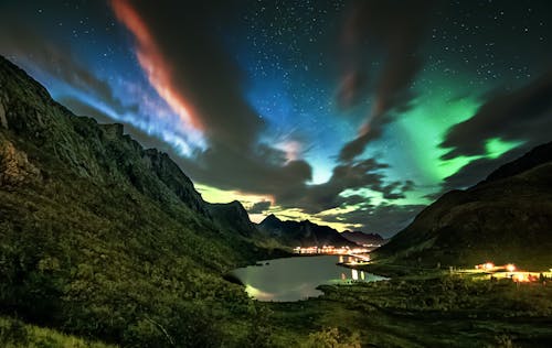 Breathtaking scenery of northern lights over Reine village located on seashore surrounded by green rocky mountains  in Norway