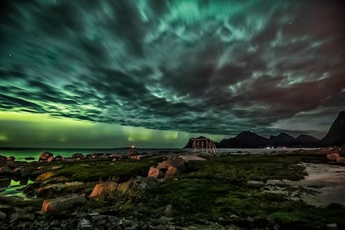 Scenic landscape of rocky seashore against cloudy sky with aurora borealis