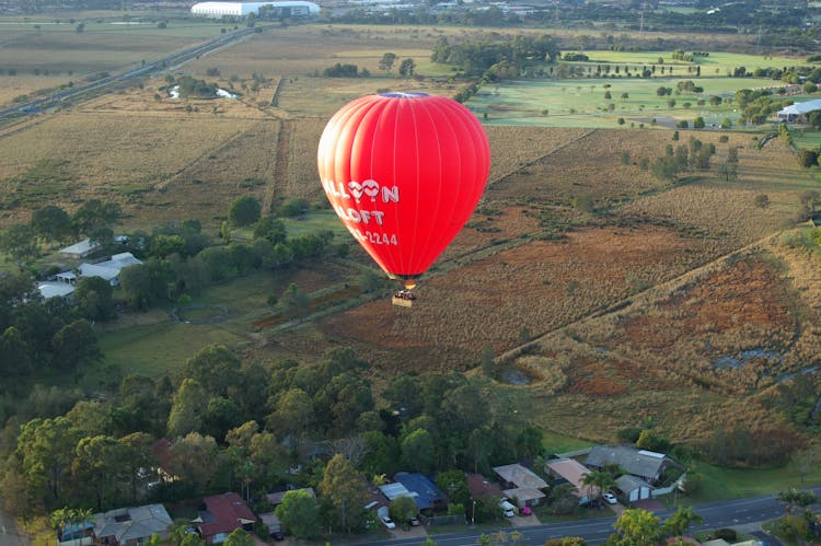 Red Hot Air Balloon Flying Over Fields