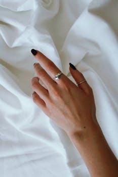 Close-up of a hand with stylish rings and black nail polish on white fabric.