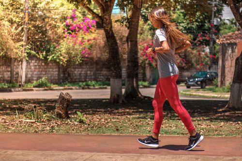 Free A woman jogs on a path surrounded by trees and vibrant flowers, embodying a healthy lifestyle. Stock Photo