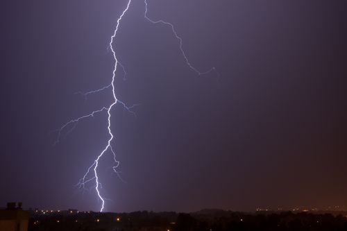 Free A powerful lightning bolt illuminates the night sky over a city skyline during a thunderstorm. Stock Photo