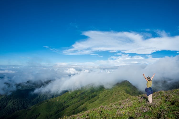 Person Standing On Peak On Mountain With Raised Hands 