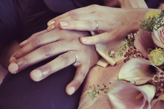 A close-up of a couple's hands wearing wedding rings, symbolizing love and commitment, surrounded by flowers.