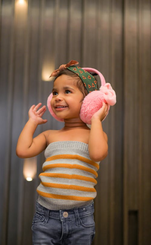 Free Positive little girl in pink earmuffs near ribbed wall Stock Photo