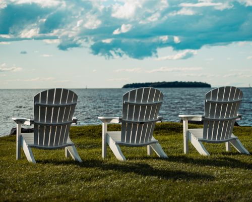 Free Three Adirondack chairs facing the ocean with a beautiful cloudy sky, perfect for relaxation and seaside enjoyment. Stock Photo