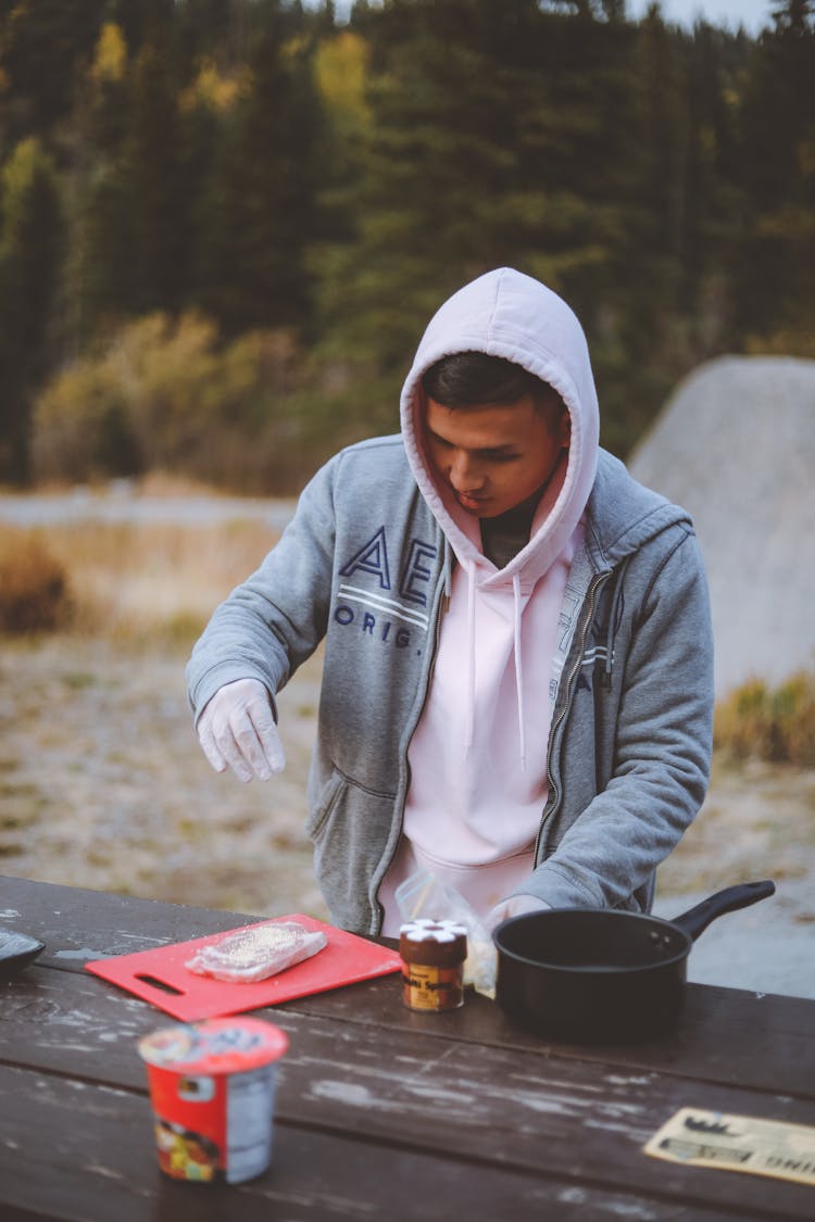 Positive Ethnic Man Salting Meat Steaks In Nature