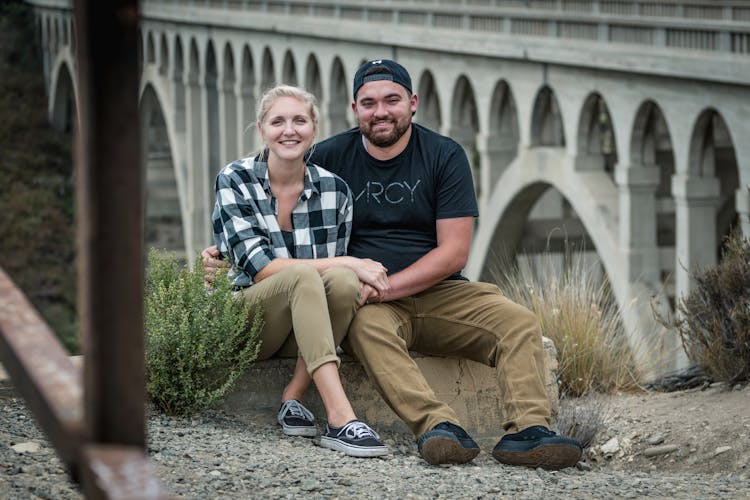 Happy Couple Sitting On Bridge Background