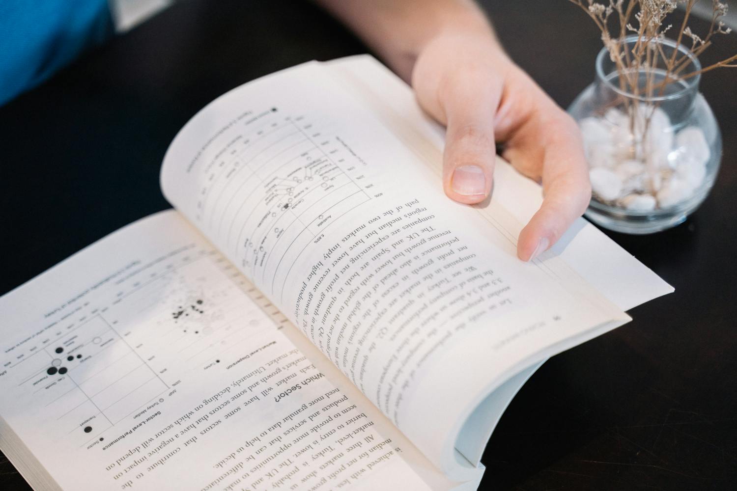 Close-up of a hand turning pages in a book with data charts and text.