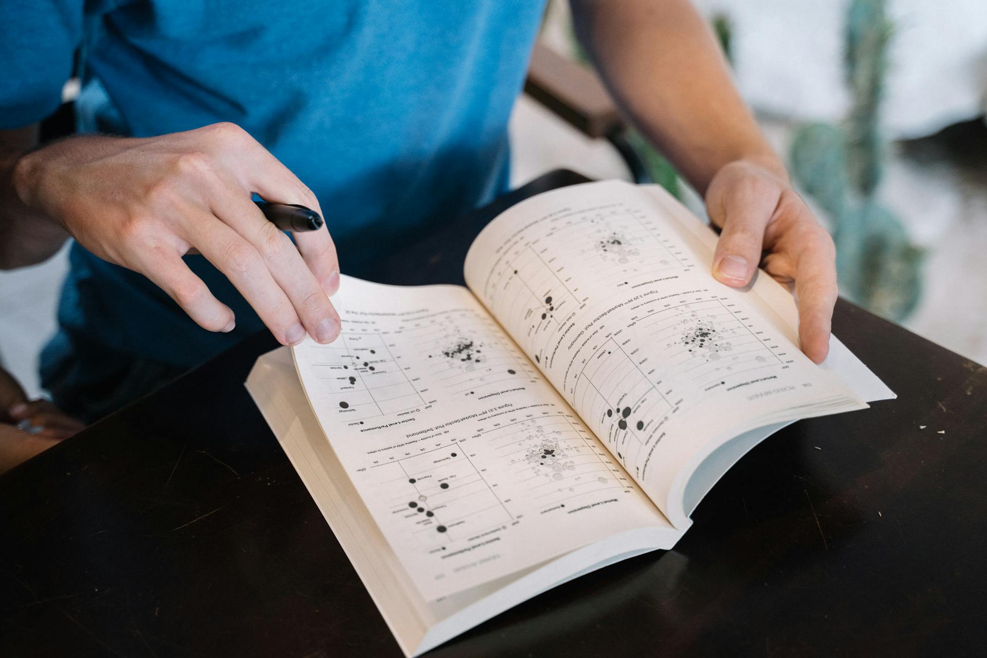 Person flipping through a textbook, examining pages with scientific graphs. Ideal for educational contexts.