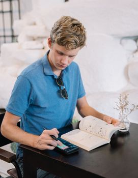 Young person in blue polo shirt studying using a book and tablet in a cozy indoor setting.