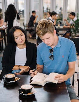 Two young adults studying together in a cozy café, engaging with books and coffee.