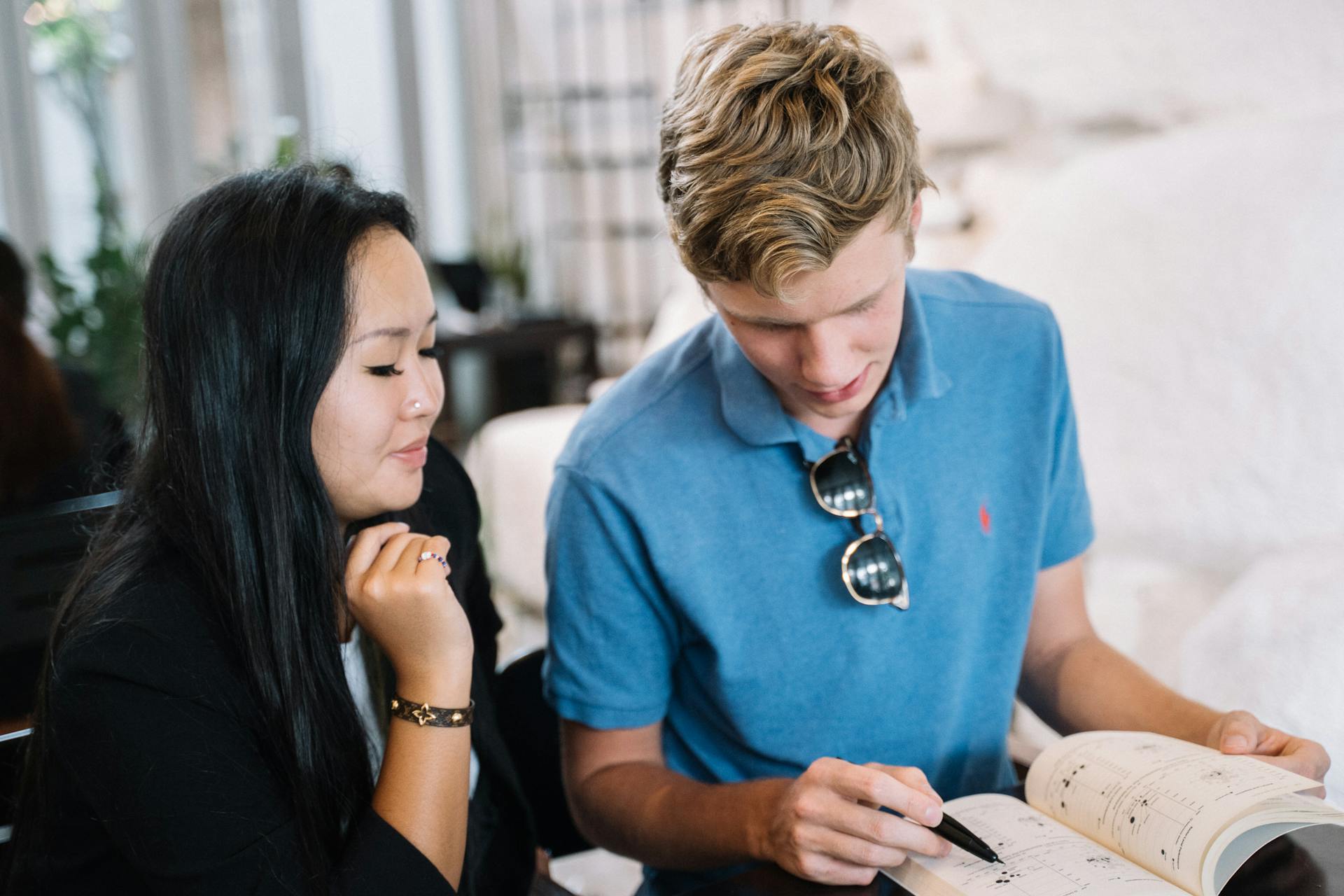 Two young adults engaged in studying together at a casual café setting, focusing on a textbook.