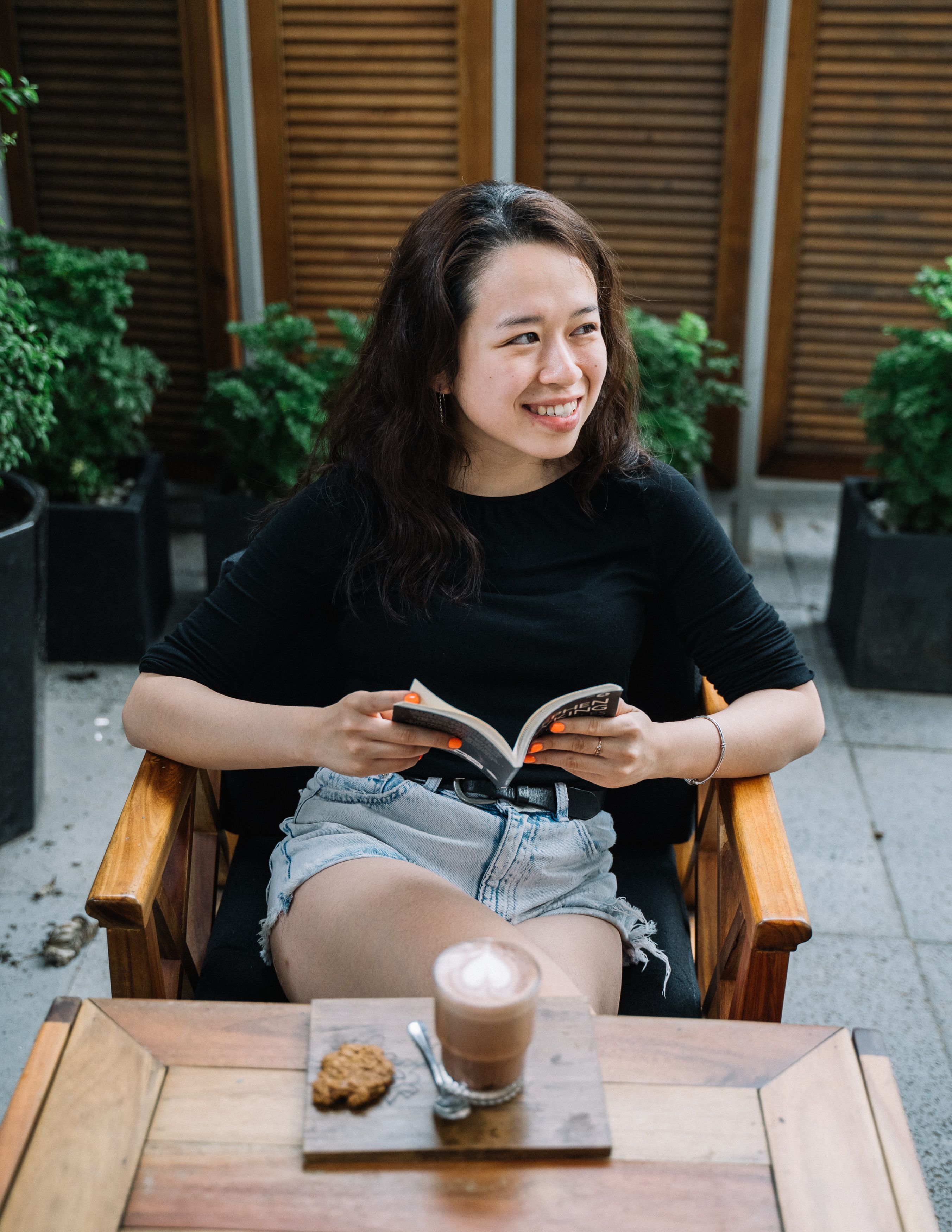 Young woman enjoying coffee and a book while sitting outdoors.