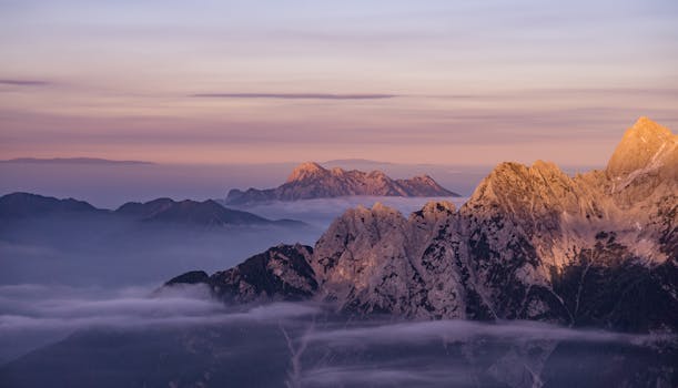 Beautiful mountain range with mist and soft sunrise hues, captured in a panoramic view.