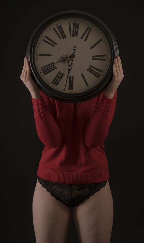Woman Wearing Underwear and Sweater Holding Clock in front of Her Face
