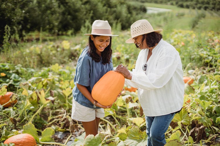 Happy Hispanic Woman With Daughter Holding Pumpkin