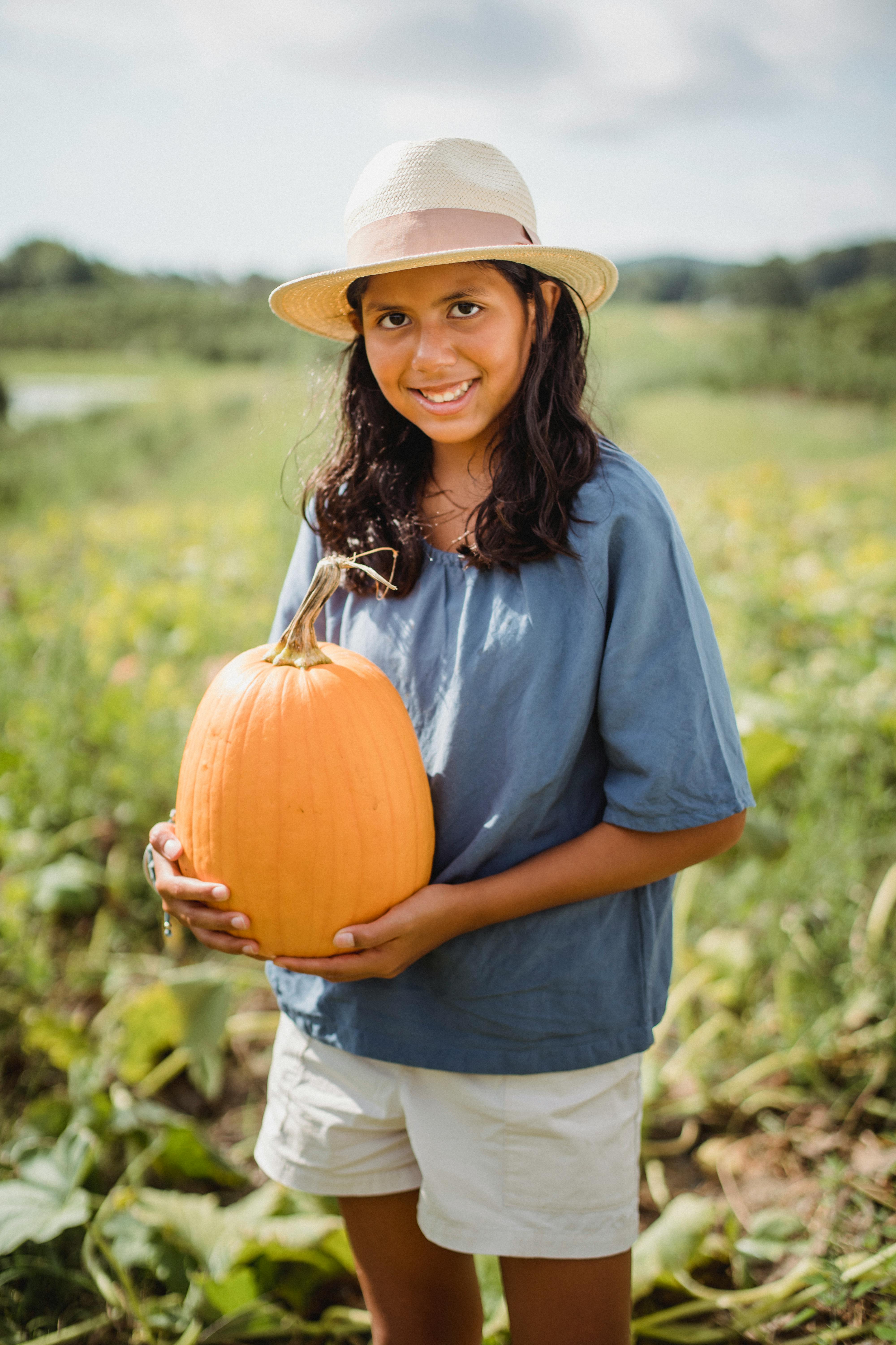 young hispanic girl holding pumpkin in field