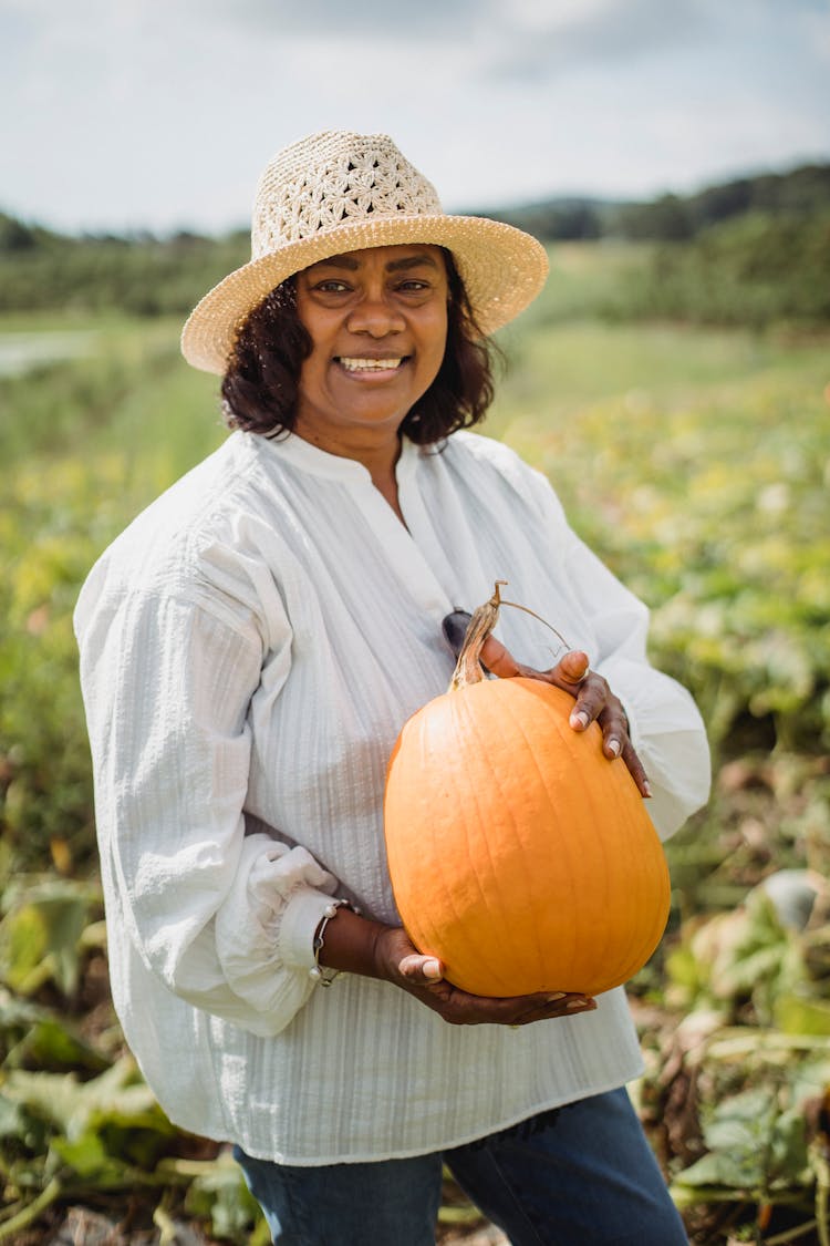 Happy Hispanic Woman Holding Pumpkin In Field