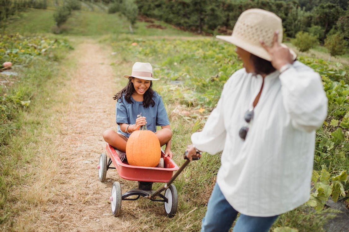 Woman rolling daughter with pumpkin in cart