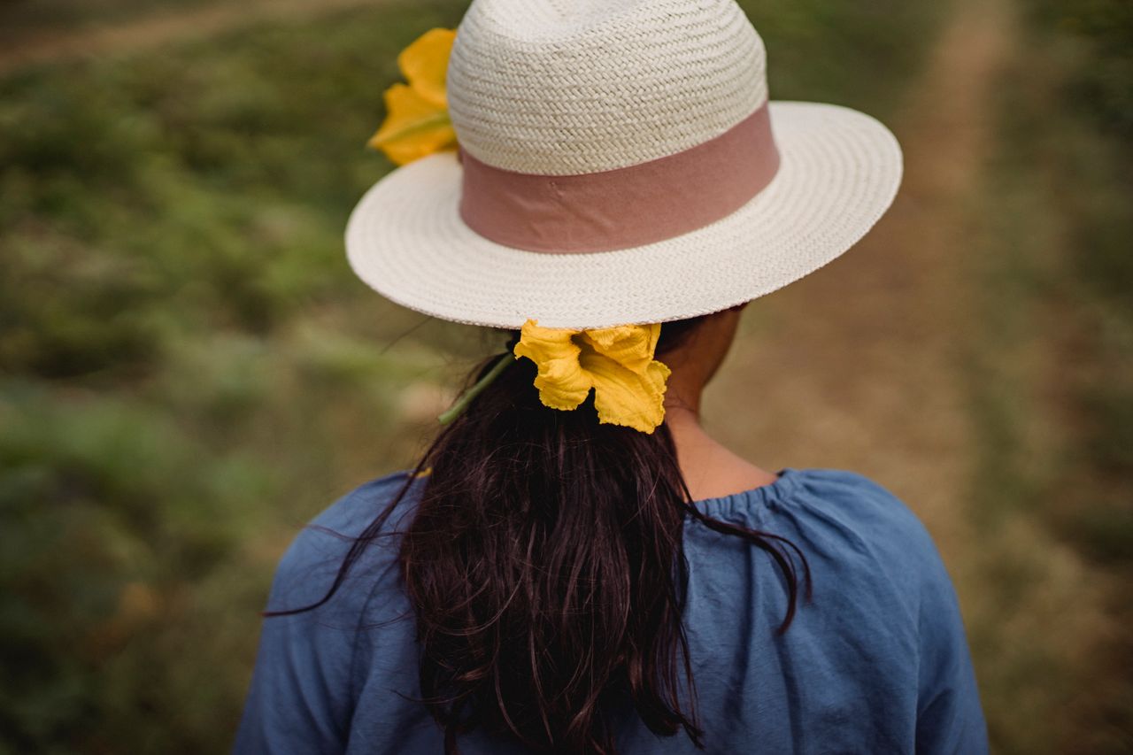 back view of faceless female in summer hat with blooming flowers in da