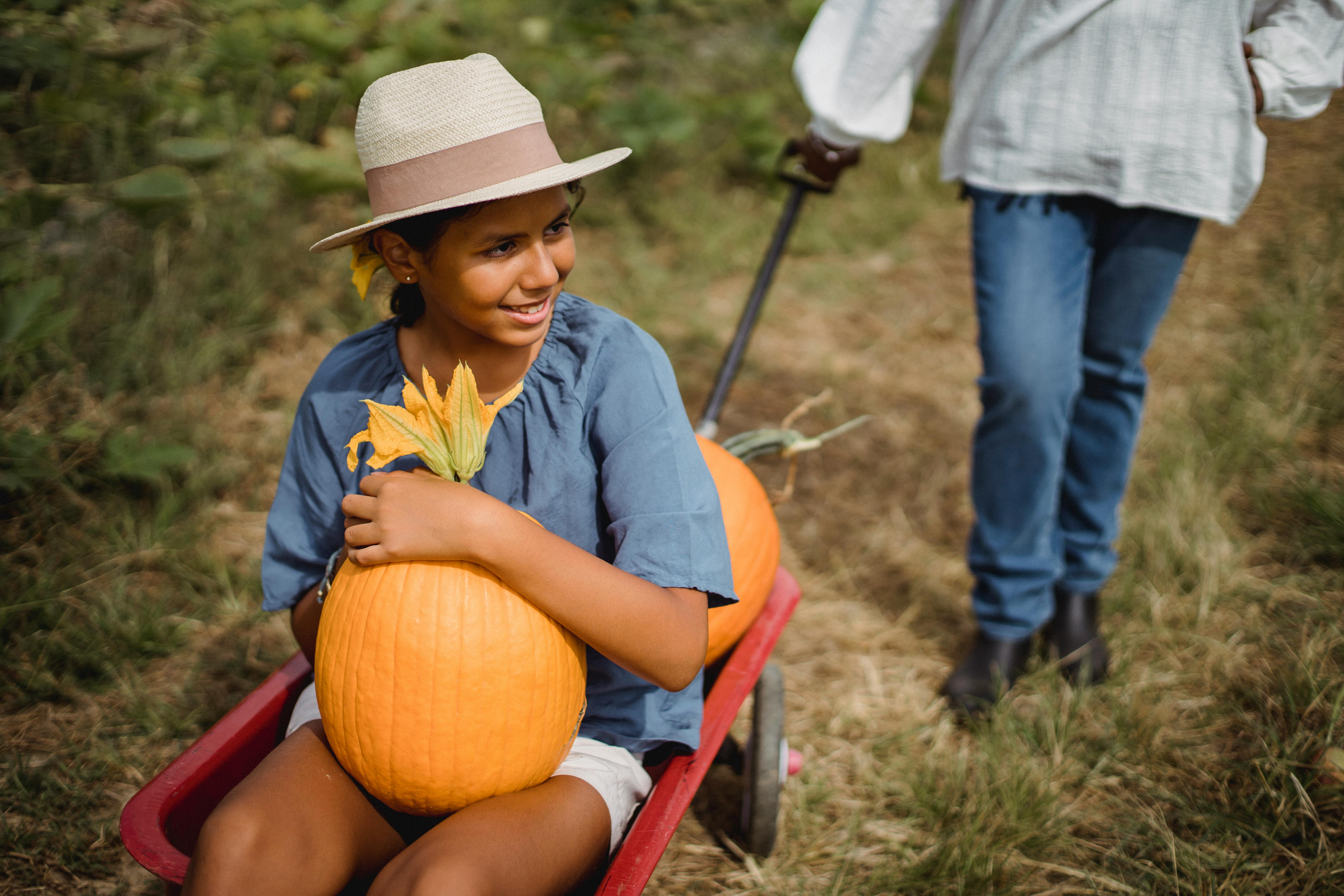 happy hispanic girl in cart with pumpkin