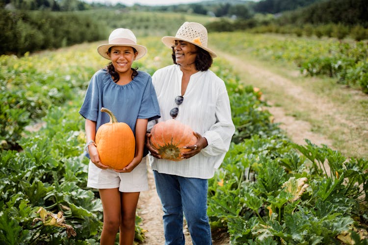 Happy Hispanic Woman With Daughter Holding Pumpkins