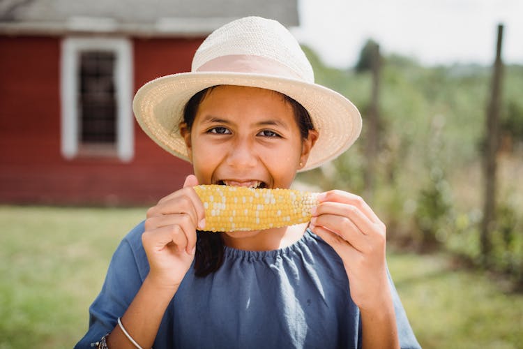 Smiling Ethnic Teen Girl Eating Corn In Countryside