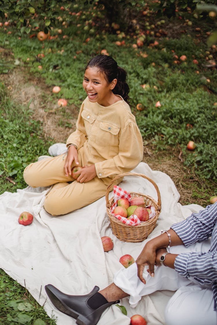 Happy Ethnic Teen Girl Laughing While Having Picnic In Garden