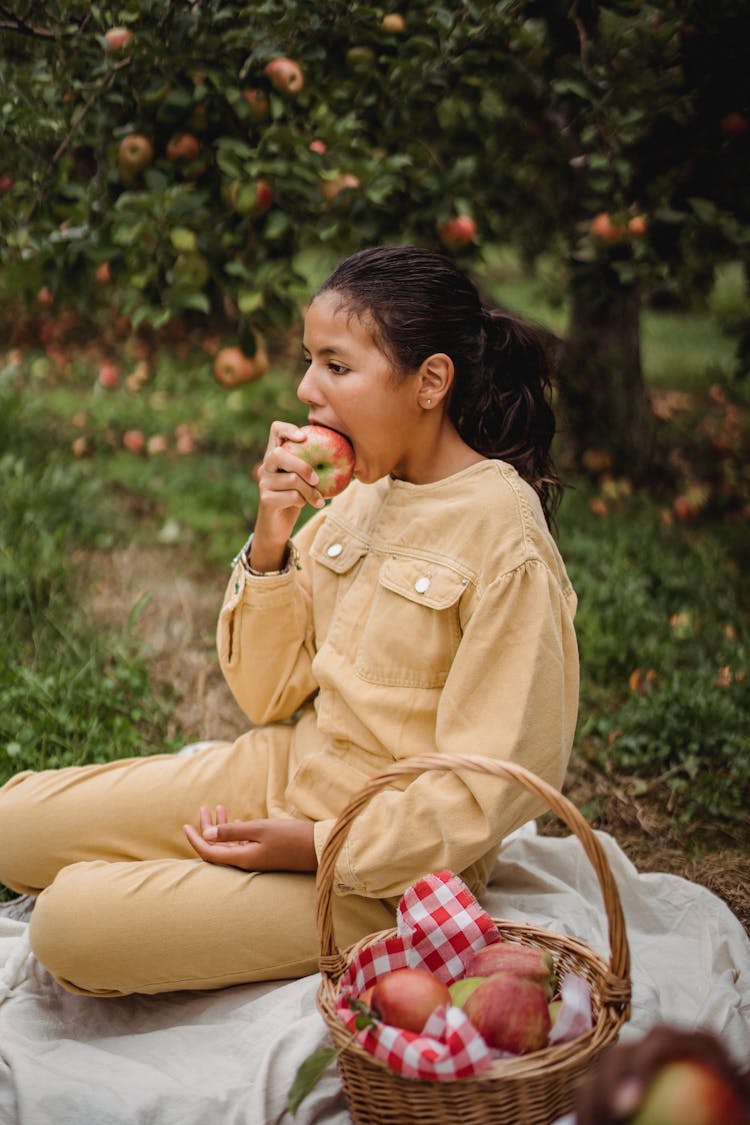 Ethnic Teen Girl Sitting On Blanket And Eating Apple