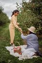 Mother giving apple to ethnic girl during picnic in orchard