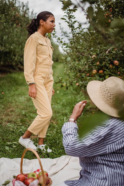 Free Side view of disappointed Hispanic teen girl standing on grass near apple trees during picnic with mother Stock Photo