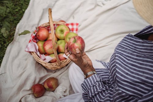 Free From above of crop ethnic female with ripe apple sitting on plaid while having picnic in nature Stock Photo