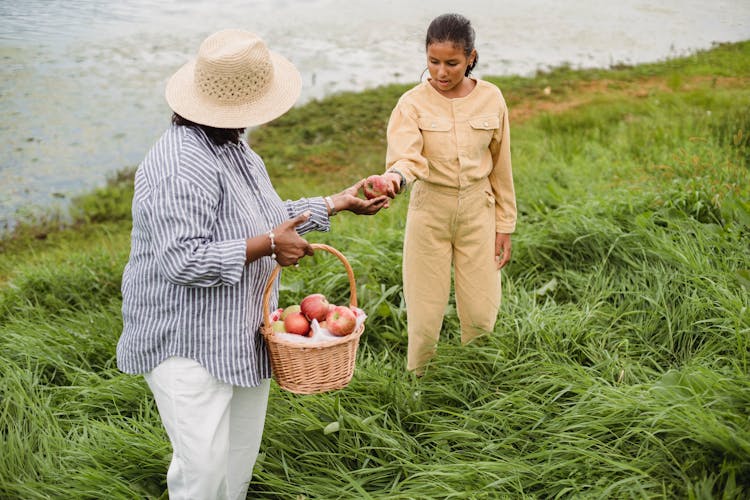 Anonymous Woman Treating Girl With Apple On River Bank