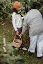 Faceless ethnic women carrying together wither basket full of ripe berries near bushes in soft daylight