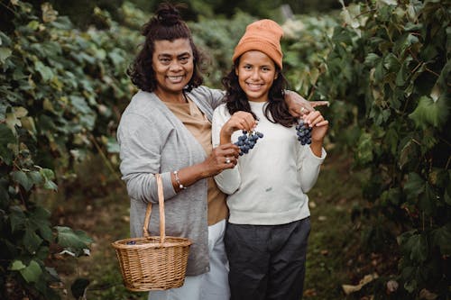 Happy ethnic woman embracing teenager with bundles of ripe grapes