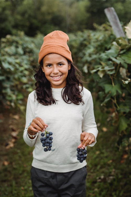 Smiling ethnic girl with bundles of grapes in vineyard