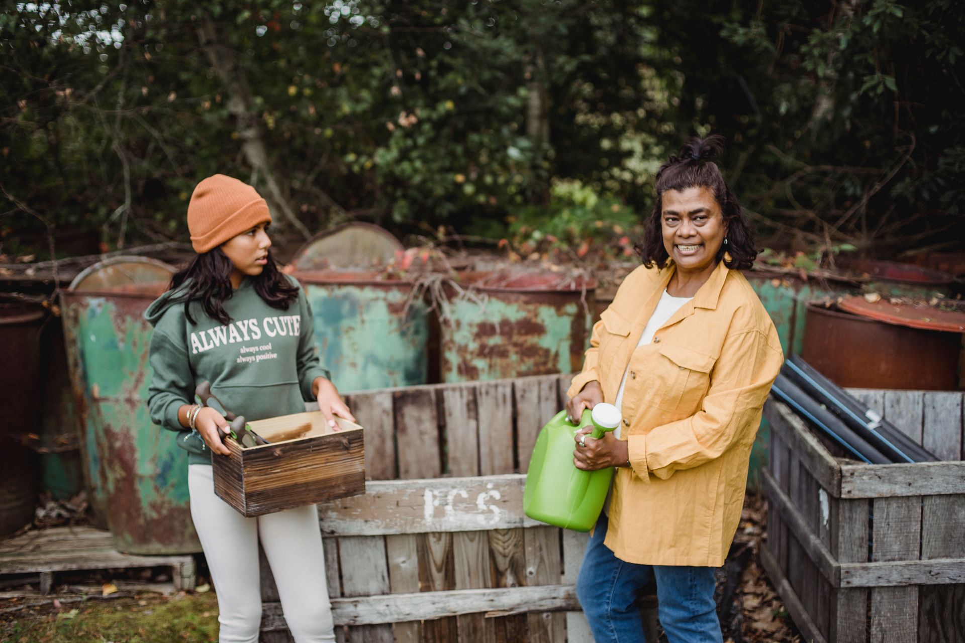 Content ethnic gardener with daughter near rusty containers on farm