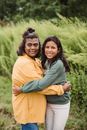 Happy ethnic mother and daughter in casual clothes embracing each other and smiling while standing in green meadow in countryside