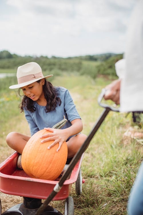 Ethnic girl with pumpkin near unrecognizable farmer in countryside