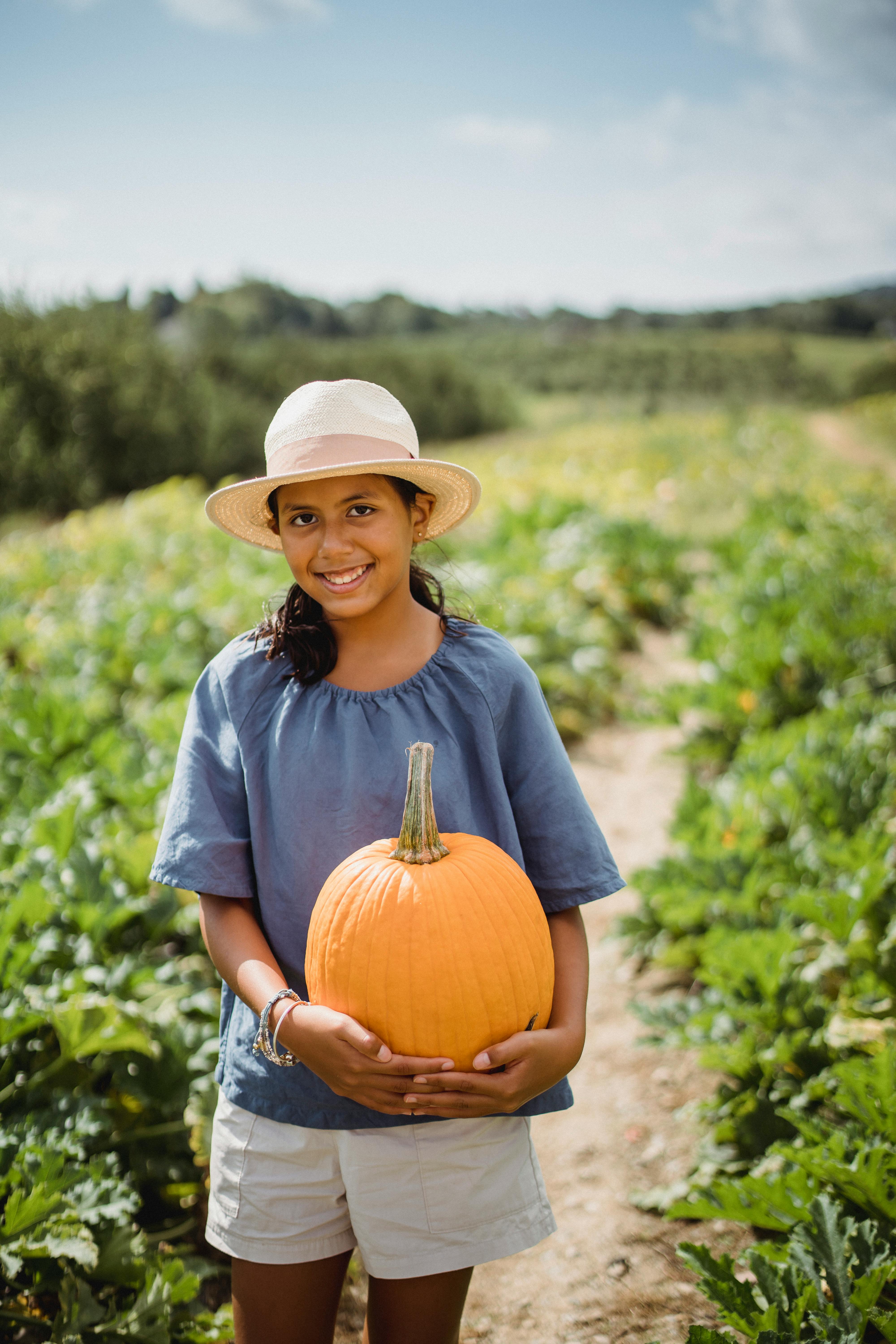 smiling ethnic farmer with pumpkin on plantation in sunlight