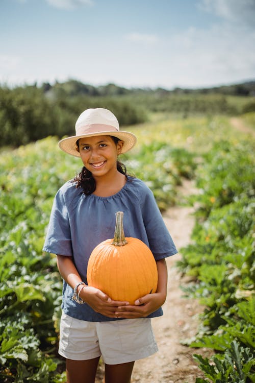 Smiling ethnic farmer with pumpkin on plantation in sunlight