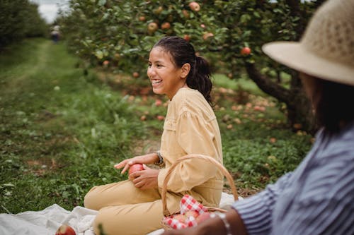 Cheerful ethnic girl near crop mother resting on grass pathway