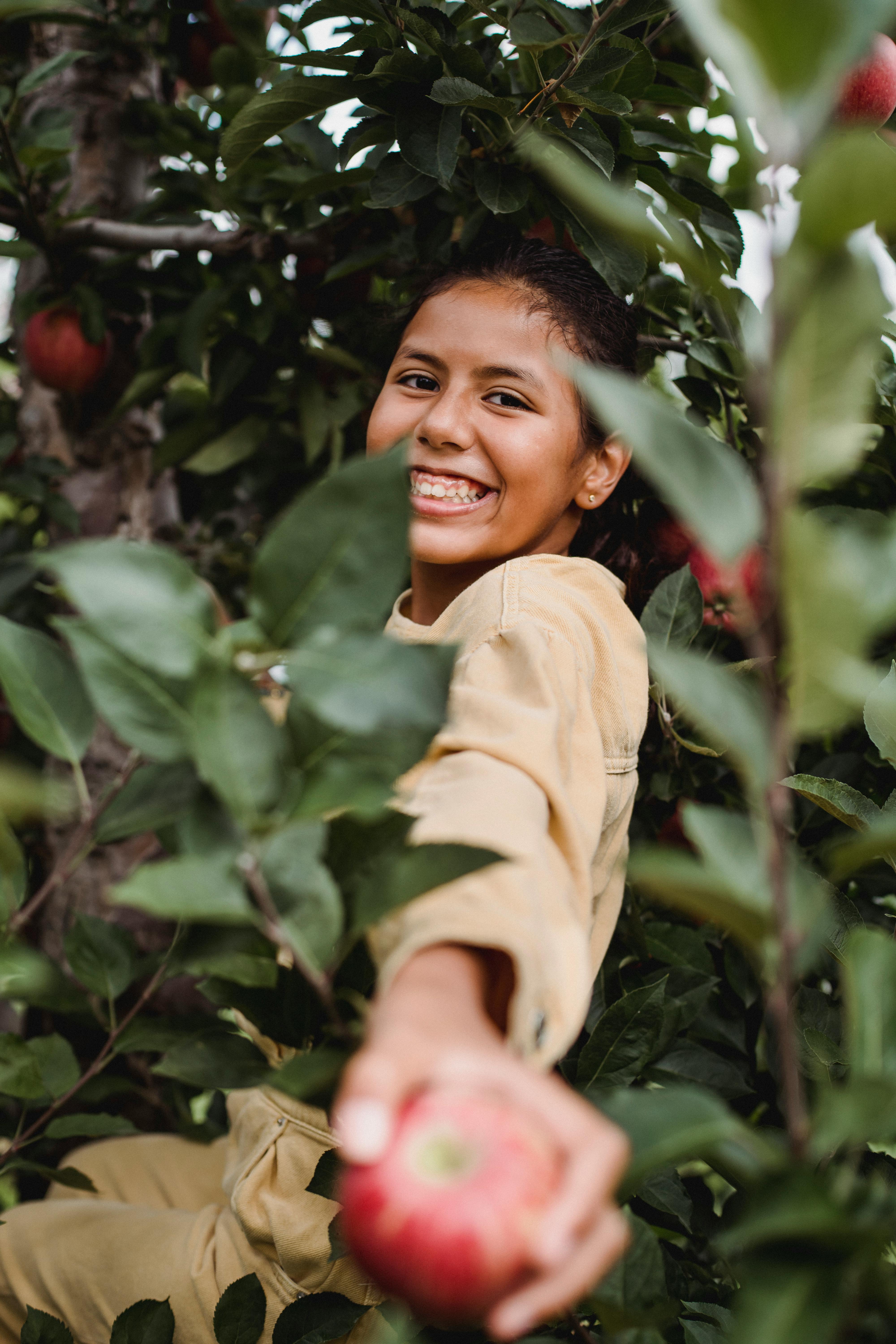 charming ethnic girl showing ripe apple among tree branches