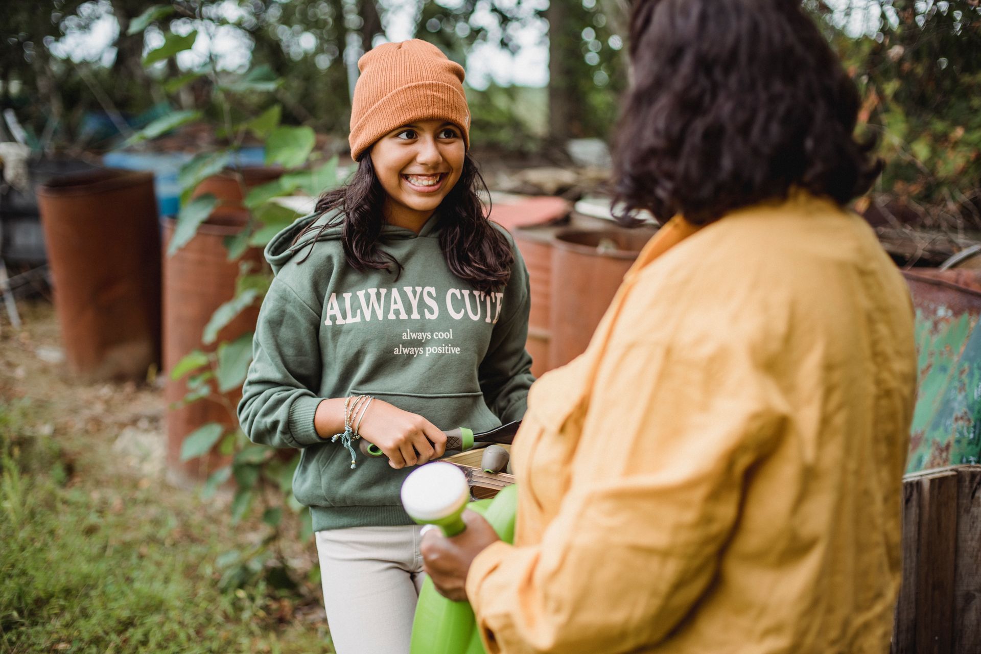 A joyful mother and daughter gardening outdoors with a watering can and tools in a casual setting.